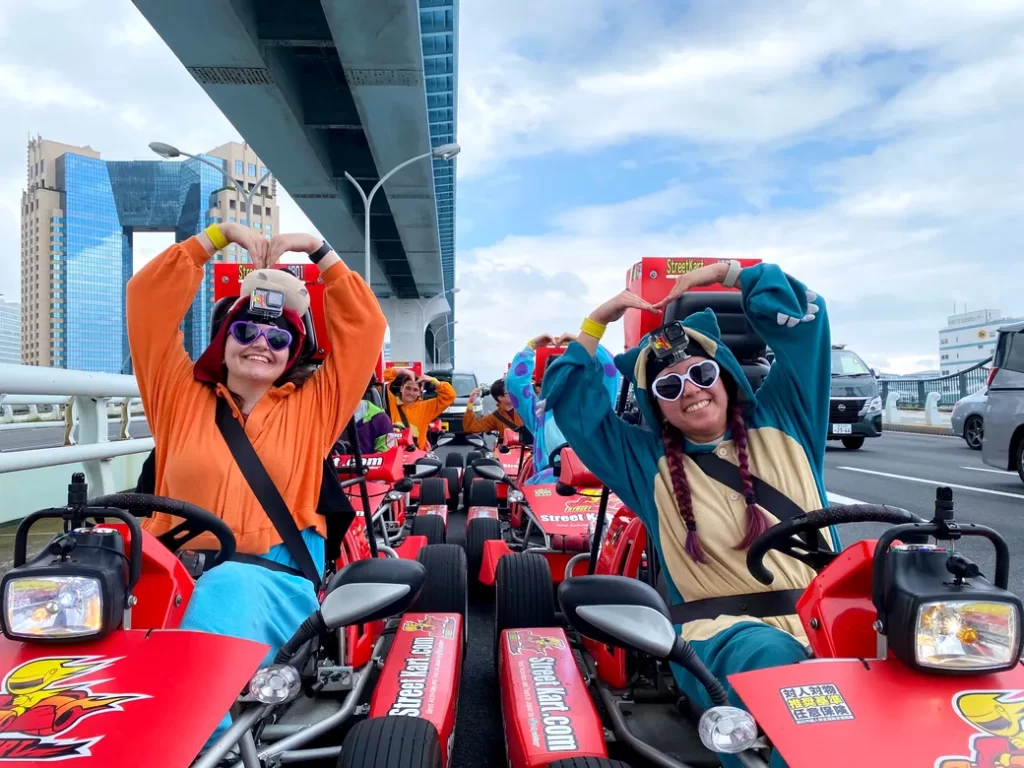 IMG_4670 - StreetKart Group of people in red go-karts on a city bridge, wearing helmets and GoPros, forming heart shapes with their arms.